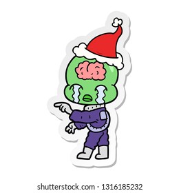 hand drawn sticker cartoon of a big brain alien crying and pointing wearing santa hat