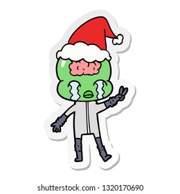 hand drawn sticker cartoon of a big brain alien crying and giving peace sign wearing santa hat