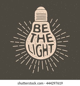 Hand Drawn Vintage Label With Textured Bulb Illustration,  Inspirational Quote And Sunburst. Be The Light. Vector Typography Poster. Lettering Artwork For T-shirt Or Bag Print