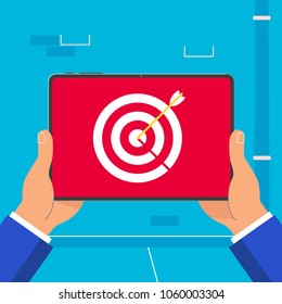 Hand holding black tablet device isolated on wall background. Pad tablet on human hands with target icon and arrow in bull eye sign on the screen flat design style vector illustration. 