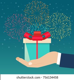 Hand holding blue gift box decorated against the background of fireworks. Vector flat illustration 