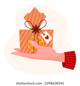 Hand holding christmas box gift cartoon vector illustration. Present in hand. Cartoon gift box decorated with slice dry orange , anise star and tag with red heart.	