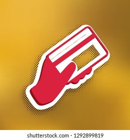 Hand holding a credit card. Vector. Magenta icon with darker shadow, white sticker and black popart shadow on golden background.