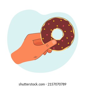 Hand holding donut with chocolate icing. Pastry with little hearts on it on blue background. Food concept for banner, website design or landing web page