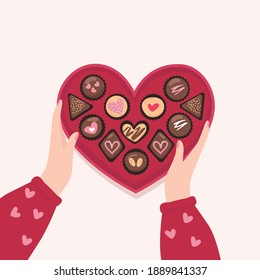mano sujetando la caja de forma del corazón con chocolate, galletas.