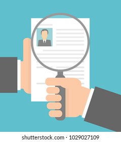 Hand holding magnifying glass over a resume or a cv . Recruitment concept