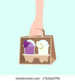 hand is holding the paper bag that has 2 juice smooties with fruit on top (apple, grape) inside. take a way beverages. home delivery concept. organic and healthy soft drink for summer.