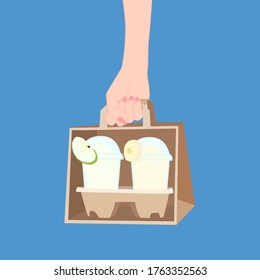 hand is holding the paper bag that has 2 juice smooties with fruit on top (apple, banana) inside. take a way beverages. home delivery concept. organic and healthy soft drink for summer.