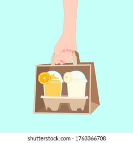 hand is holding the paper bag that has 2 juice smooties with fruit on top (orange, banana) inside. take a way beverages. home delivery concept. organic and healthy soft drink for summer.