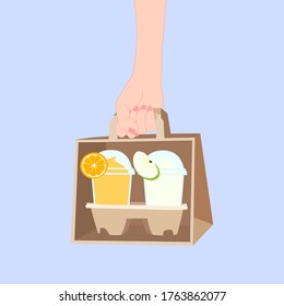 hand is holding a paper bag that has 2 juice smoothies with fruit on top (orange, apple) inside. take a way beverages. home delivery concept. organic and healthy soft drink for summer.