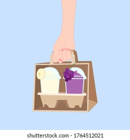 hand is holding the paper bag that has 2 juice smooties with fruit on top (banana, grape) inside. take a way beverages. home delivery concept. organic and healthy soft drink for summer.