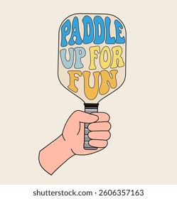 Hand holding a pickleball paddle with Paddle Up For Fun in retro-style lettering, featuring bold colors and vintage aesthetics