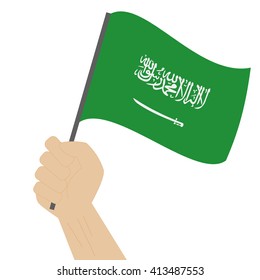 Hand holding and raising the national flag of Saudi Arabia