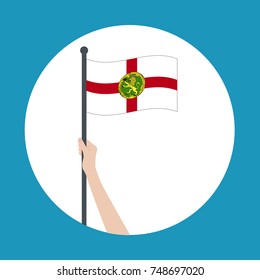 Hand holding and raising the national flag of Alderney. Hand proudly waving the national flag of Alderney.