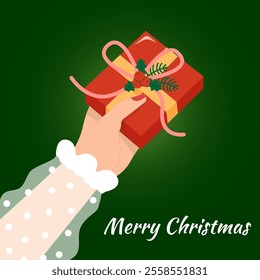 Hand holding a red Christmas gift decorated with ribbon, holly, and berries, against a green background. Flat vector illustration