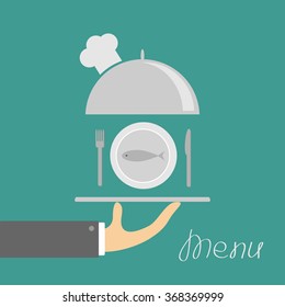 Hand holding silver platter cloche with chefs hat and plate fish, fork, knife. Menu card. Green background. Flat design. Vector illustration