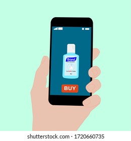 Hand holding smart phone with buy button on the screen. Contactless online purchase of goods using your phone. Use Hand Sanitizer. Alcohol gel bottle. Diseases prevention. Home delivery.