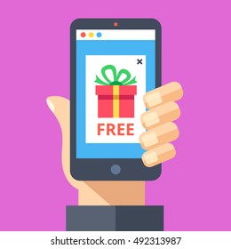 Hand holding smartphone with pop-up ad on screen with red gift and word free. Online advertising, sale, discount, promotion, internet fraud, scam concepts. Modern flat design vector illustration