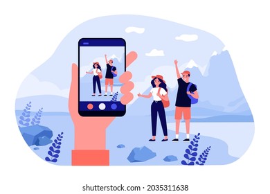 Hand holding smartphone, taking pictures of young travelers. Flat vector illustration. Man and woman posing with backpacks and mountain landscape on background. Travel, trip, photo, technology concept