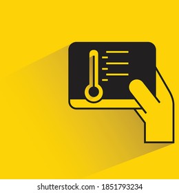 hand holding tablet controlling thermometer with shadow on yellow background