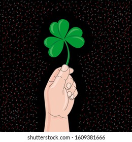 Hand holds clover on black background. St. Patrick Day Symbol