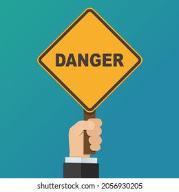 A hand holds up an orange diamond sign with the text danger on a blue background (flat design)