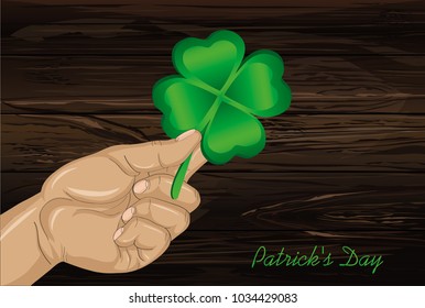 Hand holds ornate clover four-leaf. Celebration concept St. Patrick's Day. Greeting card. Vector illustration on a wooden background. Free space for your text and labels.