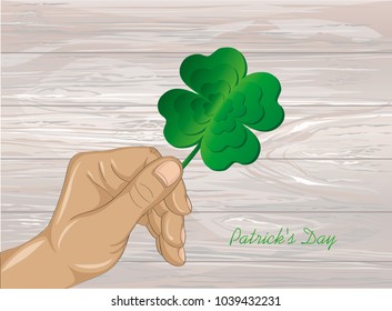 Hand holds ornate clover four-leaf. Celebration concept St. Patrick's Day. Greeting card. Vector illustration on a wooden background. Free space for your text and labels.