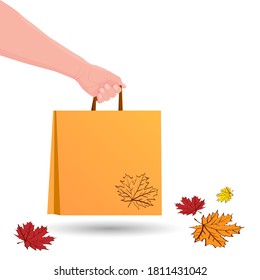 Hand holds shopping bag. Food delivery in paper packet. Shopping or gift bag. Eco Bag mockup Isolated on white background. Autumn sale concept. Colorful leaves. Vector illustration.