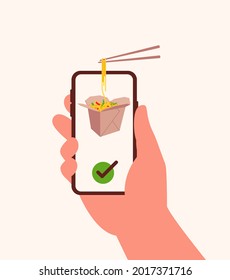 Hand holds smartphone with asian noodle with vegetables in paper box and chopsticks with noodles on screen. Concept online delivery food at home