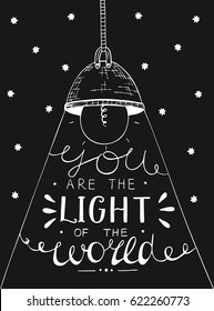 Hand lettering You the light of the world, made on black star background with glowing light bulb. Biblical background. Christian poster. New Testament