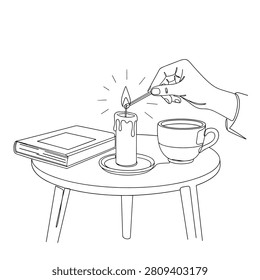 A hand lights a candle with a match on a round table, next to a book and a cup, in a cozy minimalist setting