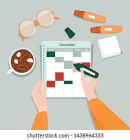 The hand make a note in the schedule, a coffee,  the stationery are around it.