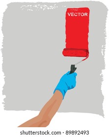 Hand with roller dipped in red colors paints grey background
