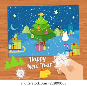 Hand with snowflake and New Year greeting card with decorated christmas tree, snowmans and gifts against the background of glowing windows of a night city