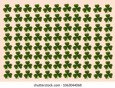 A hand-drawn stylish background arranged in rows of green leaflets of the Irish clover symbol of luck on a soft pink background