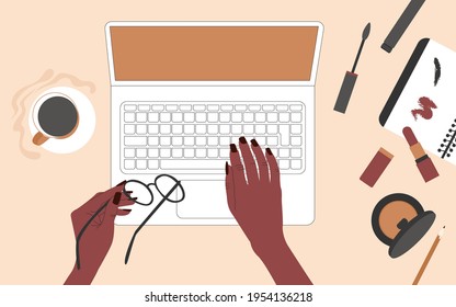 Hands of an African American woman behind a laptop. There is coffee and women's make-up supplies on the table. Top view. Flat vector illustration