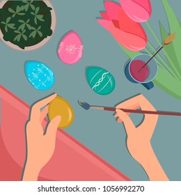 hands color Easter eggs on the table