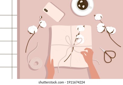 Hands and gift box on the table. Craft paper box decorated cotton heads. Top view table with items: gift box, scissors and cotton heads. Flat cartoon vector illustration isolated on pink background.
