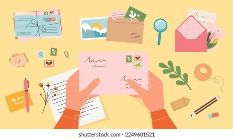 Hands holding closed envelope with stamps. Handwritten letter, postcards, photo card, labels, office supplies point of view yellow background. The concept of sending letters and postcards to a friend.