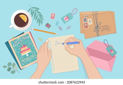 Hands holding the pencil and writing on the paper sheet. Top view of desk with envelopes, post cards, post stamps and cup of coffee