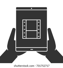 Hands holding tablet computer glyph icon. Watching films. Silhouette symbol. Tablet computer with video tape. Negative space. Vector isolated illustration