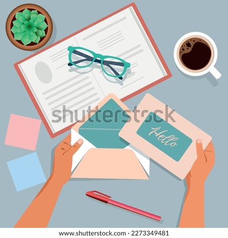 Hands on the table tear off an envelope with a postcard. Top view. Notepad, pen, glasses, coffee cup, flower.	