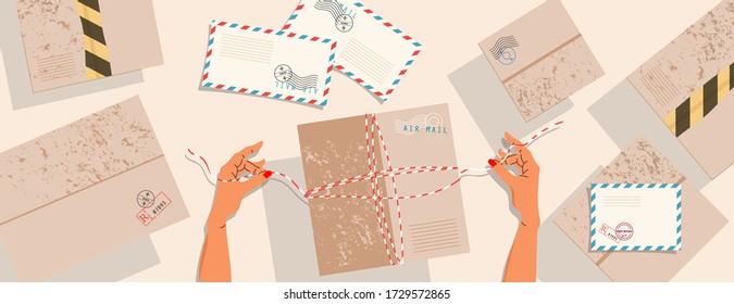 Hands and parcels on the table. Top down view. Delivery boxes, postcards with stamps and envelopes on the table. Hands tie a string and preparing the box for shipping. Parcel delivery and postage. 
