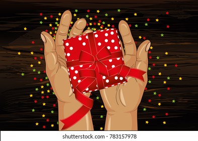 Hands stretch a gift box with a bow. View from above. Greeting card or invitation for the holiday on wooden background with confetti.