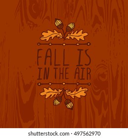 Hand-sketched typographic element with acorns and text on wooden background. Fall is in the air