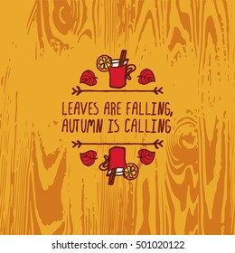 Hand-sketched typographic element with mulled wine, leaves and text on wooden background. Leaves are falling autumn is calling