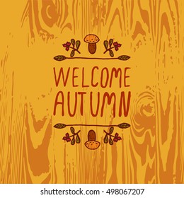 Hand-sketched typographic element with mushroom, berries and text on wooden background. Welcome autumn