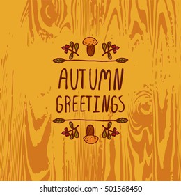 Hand-sketched typographic element with mushroom, berries and text on wooden background. Autumn greetings