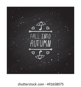 Hand-sketched typographic element with umbrella, hearts and text on chalkboard background. Fall into autumn